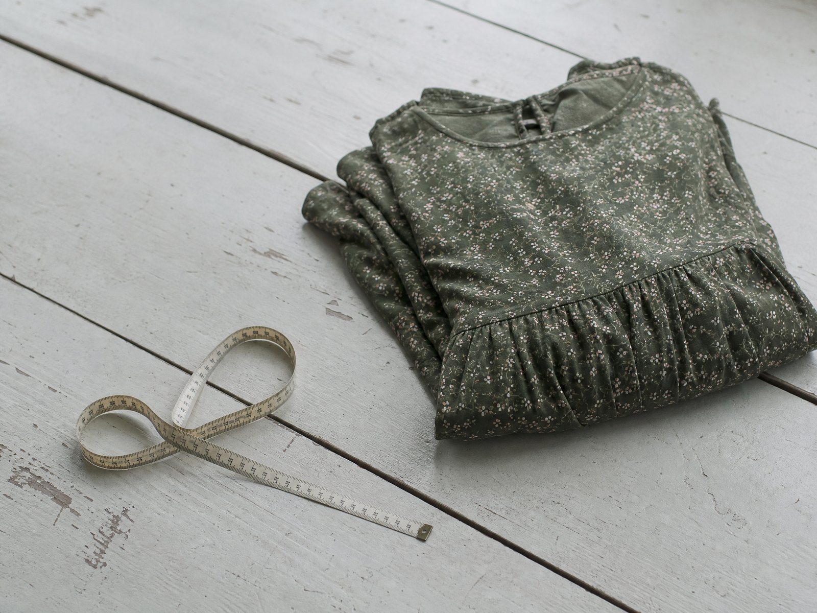 A folded ribbed knitted sock beside an uncoiled cloth tape measure